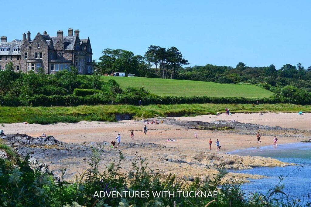 The serene North Down Coastal Path along the Irish Sea, framed by lush greenery and a historic building in the distance, a perfect walk for Instagrammable discoveries in Northern Ireland.