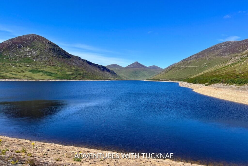 The serene waters of Silent Valley, flanked by the smooth slopes of the Mourne Mountains, reflect the clear blue sky, epitomizing the tranquil beauty of Northern Ireland's Instagrammable landscapes.
