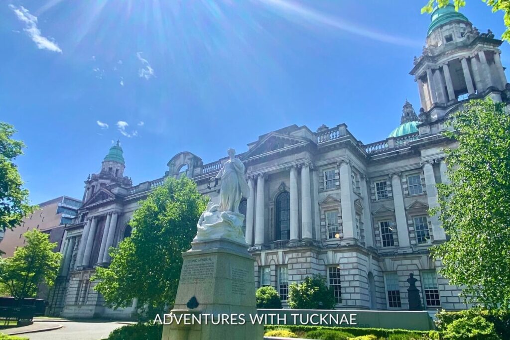Sunlight beams over Belfast City Hall and the Titanic Memorial, highlighting the grandeur of the building and the statue's details, a perfect spot for Instagram in Northern Ireland.