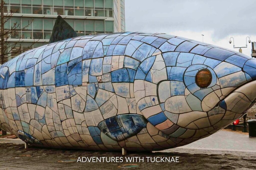 The Big Fish sculpture, also known as The Salmon in Belfast, adorned with blue and white tiles featuring printed texts and images, a unique and Instagrammable backdrop in Northern Ireland.