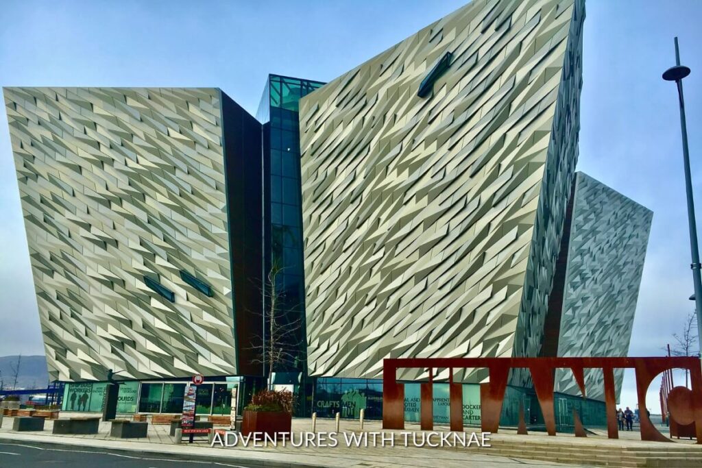 The iconic Titanic Museum in Northern Ireland, with its angular, modern design resembling a ship's hull, stands against a clear blue sky, offering an Instagrammable moment of architectural wonder.