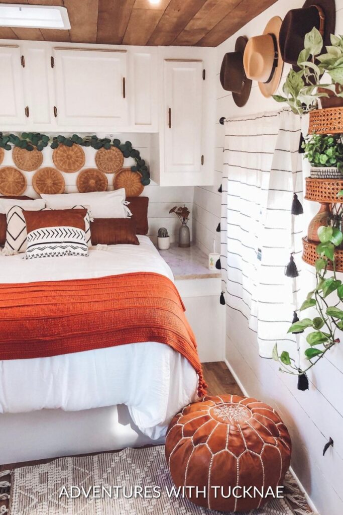 Bohemian-style RV bedroom remodel with white cabinets and a rust orange throw on the bed.