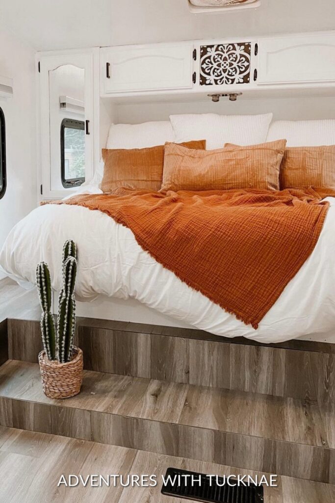 Bohemian-style RV bedroom makeover with white walls and cabinets and orange/brown colored bedding