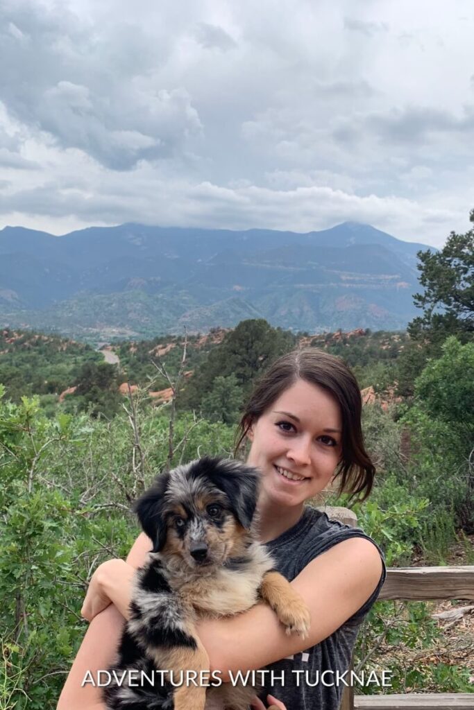 Janae holds a young Cap in her arms with a scenic mountain range in the background.