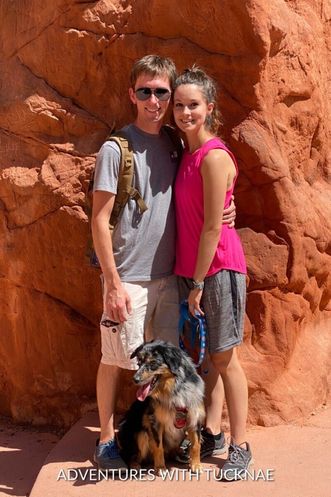 Tucker and Janae pose with Cap in front of a striking red rock formation, smiling for the camera.