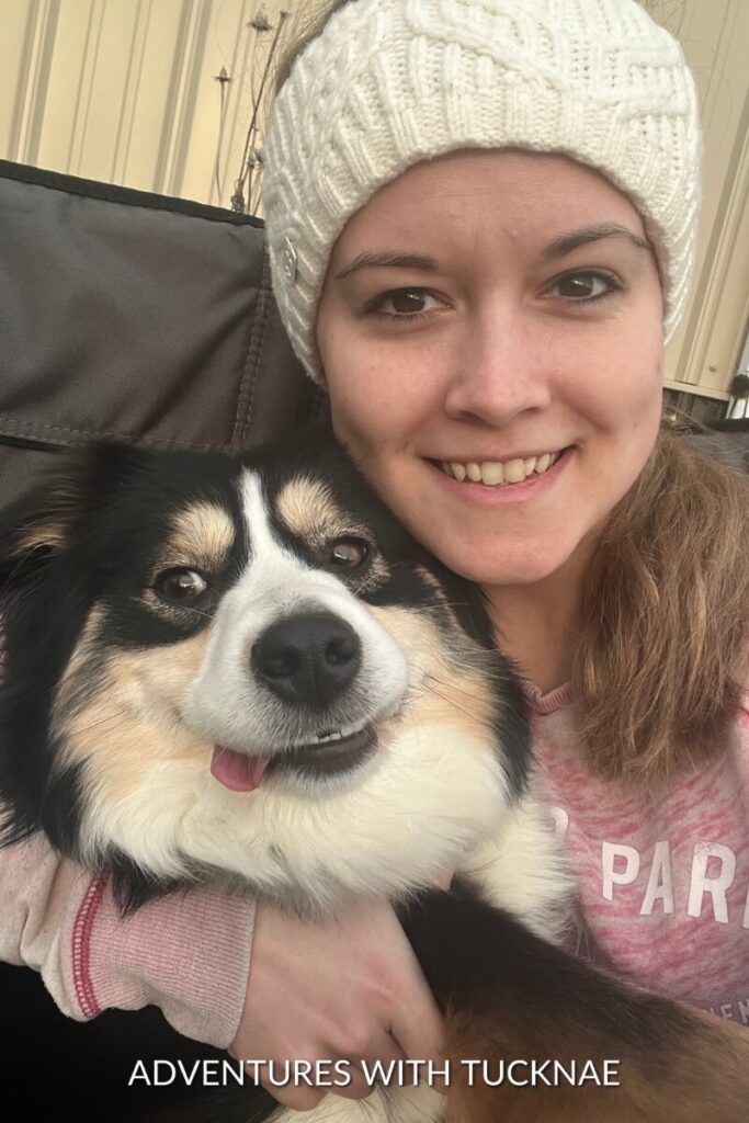 Janae wearing a white knit headband hugs Marvel, who has a happy expression, sitting outside in a camping chair by the fire.