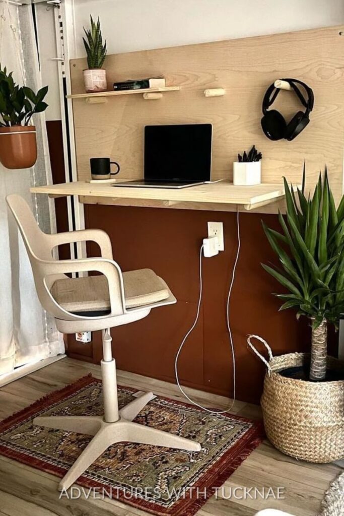 A compact RV office setup with a beige swivel chair and a wooden desk. The desk features a laptop, coffee mug, headphones, and small plants, showcasing an efficient workspace within an RV.