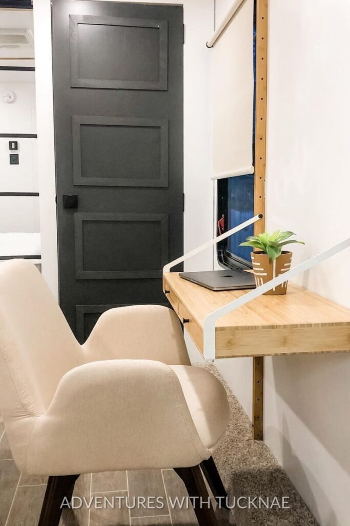 A minimalist RV office design with a beige chair and a floating wooden desk attached to the wall. A small plant sits next to the laptop, offering a clean and compact workspace that exemplifies practical RV office ideas.