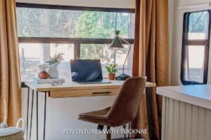 A stylish RV office setup with a mid-century modern desk and chair, featuring warm, earthy tones. The desk is accessorized with a potted plant, lamp, and notebook, making it a perfect example of chic RV office setup ideas.