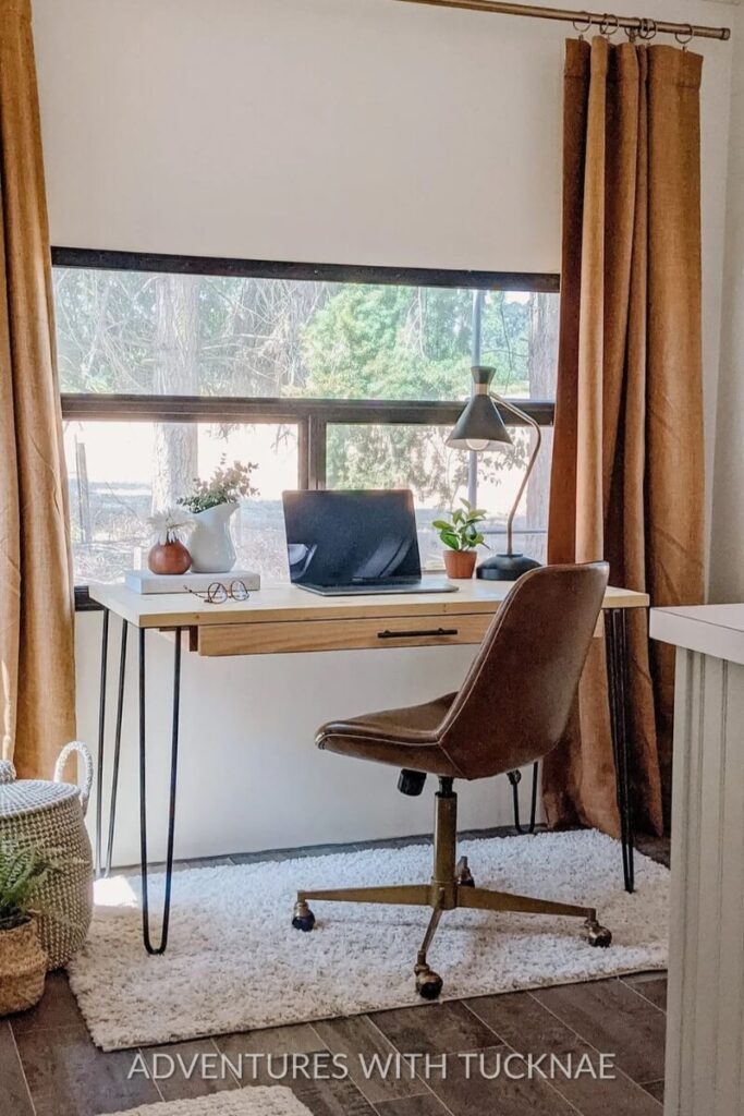 A stylish RV office setup with a mid-century modern desk and chair, featuring warm, earthy tones. The desk is accessorized with a potted plant, lamp, and notebook, making it a perfect example of chic RV office setup ideas.