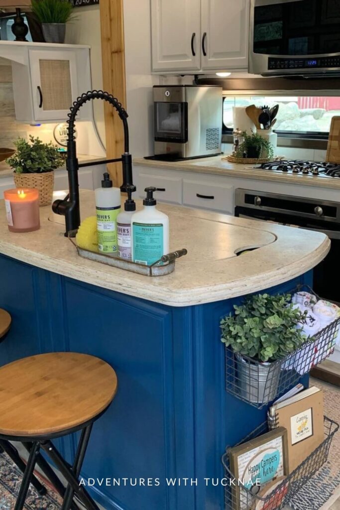 A cozy RV kitchen corner with a curved blue counter and a lit candle, with a backdrop of white cabinets and a microwave above the gas stove.