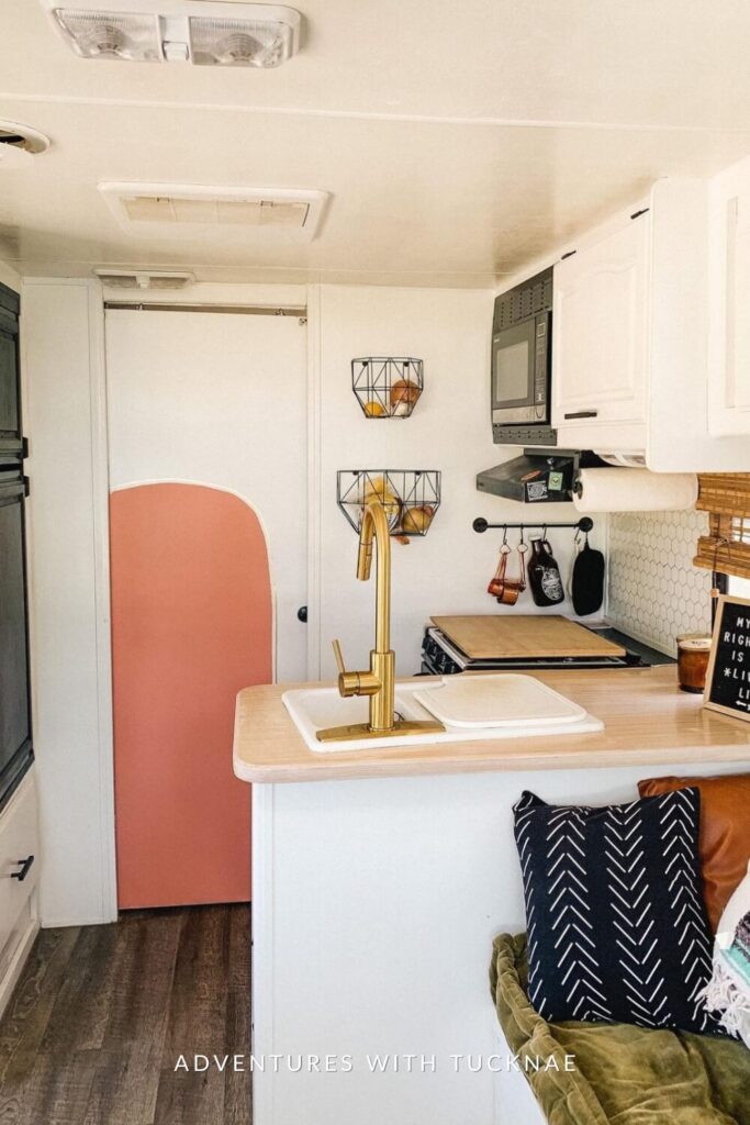 A stylish RV kitchenette with a golden faucet, white countertops, a microwave, and a sign reading 'My vibe right now is just living life', adding a personal touch.