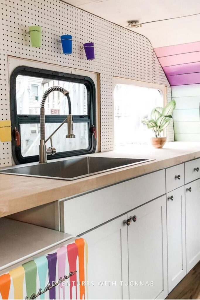 A modern RV kitchen workspace with white cabinets, a pegboard with colorful containers, and a multicolored bench, showcasing a bright and organized cooking area.