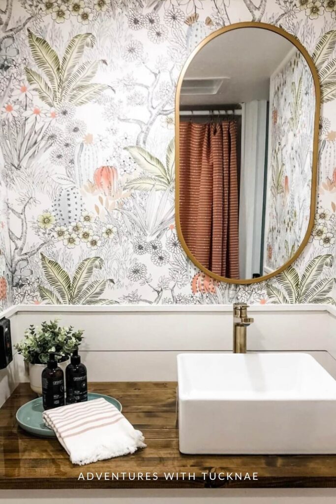 A botanical-themed RV bathroom with a vibrant floral wallpaper, a circular mirror, a modern white sink, and natural wood accents creating a refreshing space.