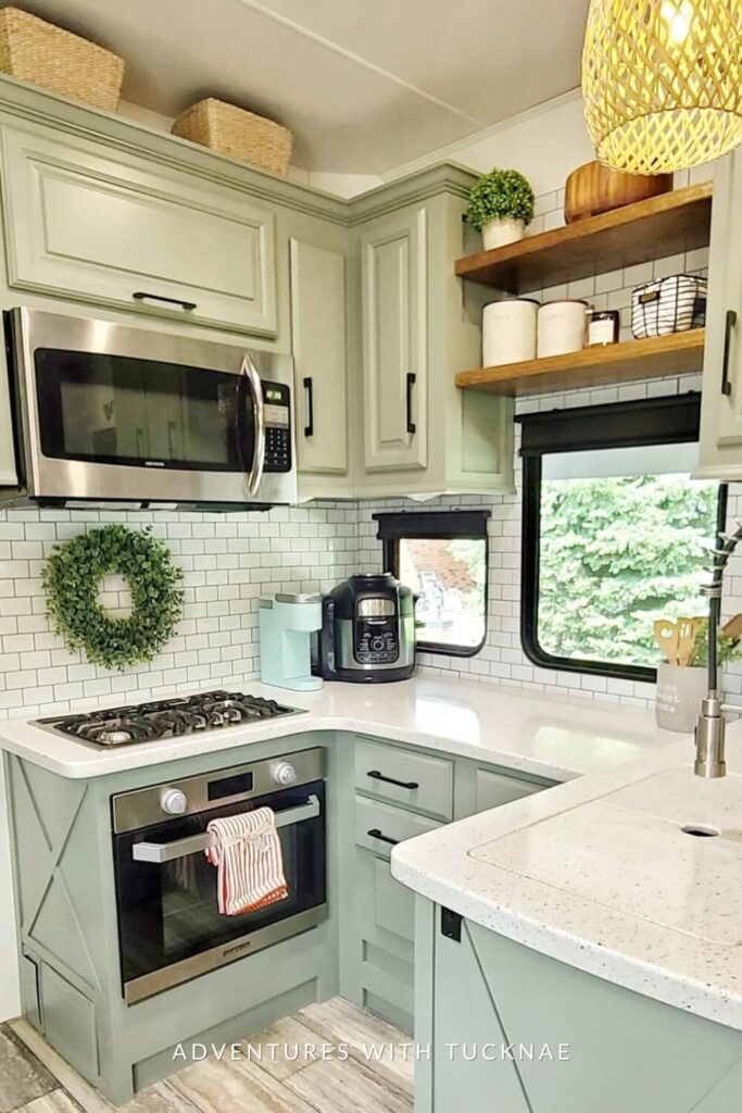 Bright RV kitchen area with white subway tile backsplash, a green wreath on the wall, stainless steel microwave above a gas stove, and a coffee maker on the counter.
