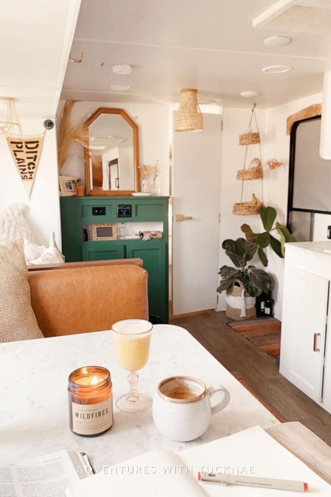 A welcoming RV living area with a green cabinet, wicker mirror, hanging plant baskets, and a cozy sofa, creating a warm and inviting space.