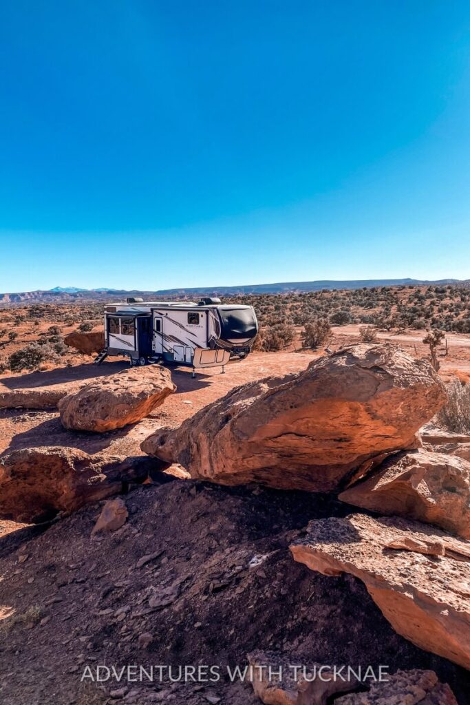 A fifth wheel RV is parked among massive red rock formations and desert vegetation under a bright blue sky in Capitol Reef National Park. This arid, scenic landscape offers a contrasting beauty among fall RV destinations.